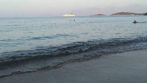 A calm sea with a boat in the distance and a person swimming.