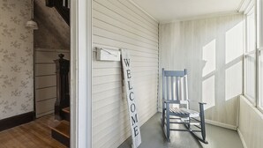 A hallway with a 'WELCOME' sign, a rocking chair, and a staircase leading to another room.