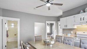 A modern kitchen with white cabinets, a wooden dining table, and a ceiling fan.