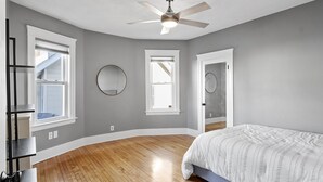A bedroom with a ceiling fan, two windows, a door, and a bed.