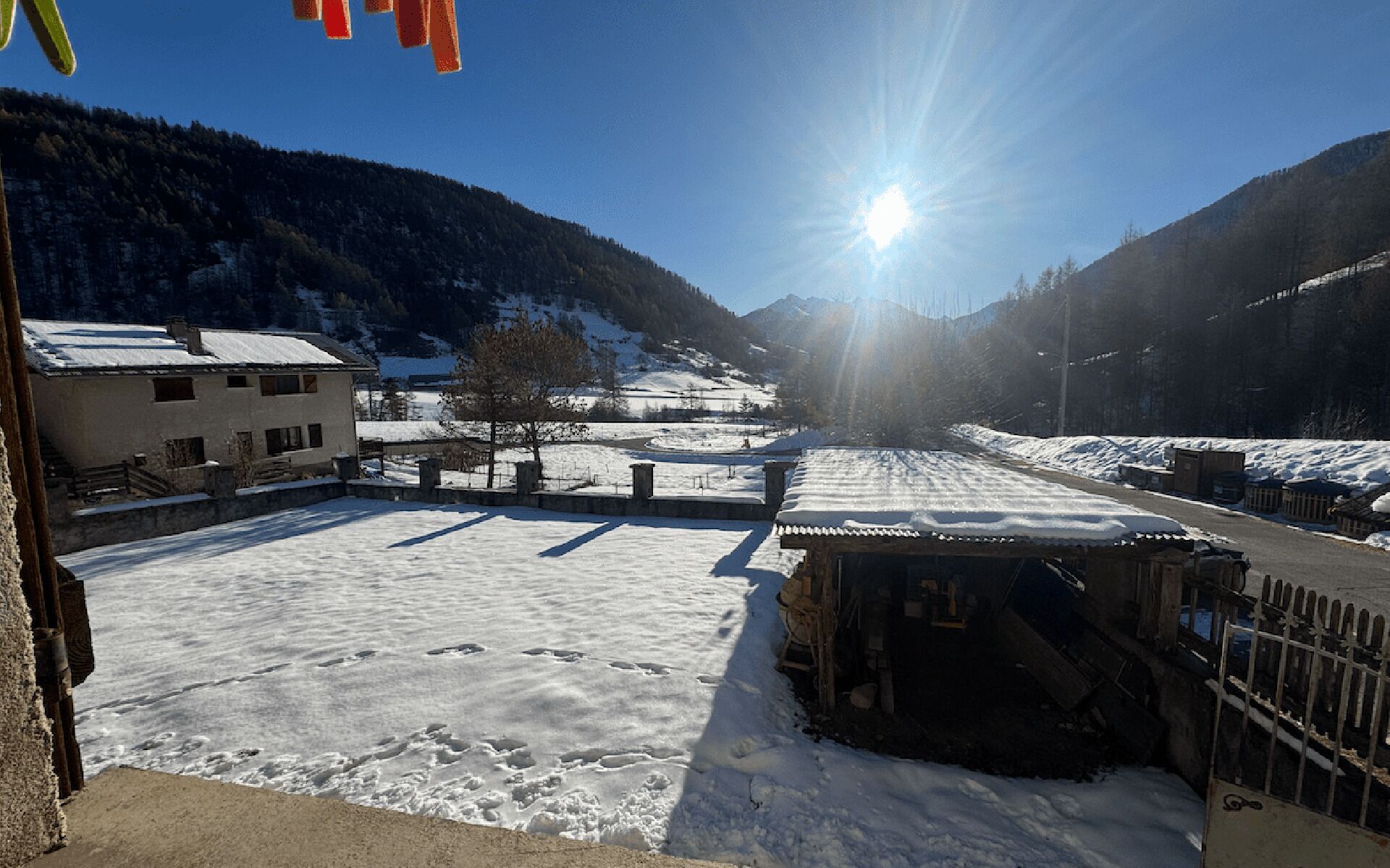 A snow-covered landscape with a building, a wooden structure, and a clear sky.
