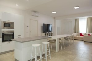 Una cucina moderna con isola centrale, sgabelli da bar, tavolo da pranzo, forno a incasso, microonde e TV a schermo piatto.