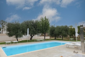 A swimming pool with lounge chairs and umbrellas, surrounded by trees and a clear sky.