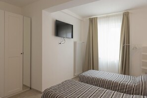 A hotel room with two beds, a television, a radiator, and a window with curtains.