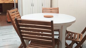 Une table de salle à manger ronde, entourée de quatre chaises en bois, recouverte d’une nappe blanche, et agrémentée d’un panier posé sur la table.