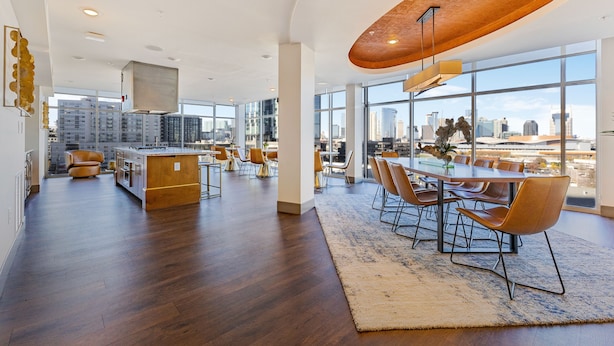 Una cocina amplia con una isla central, ventanas grandes que ofrecen vistas a la ciudad y un comedor con sillas modernas.