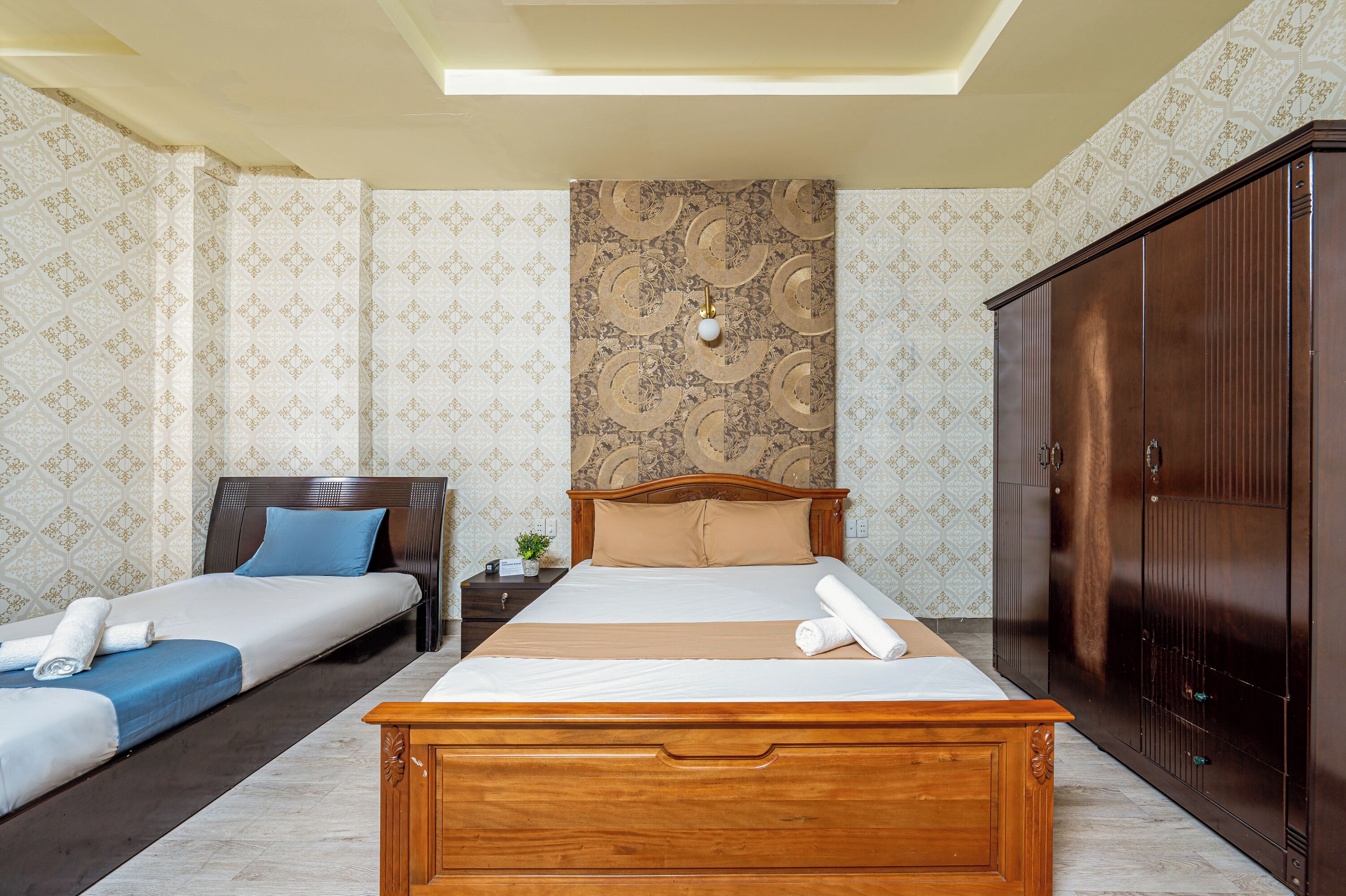 Une chambre d’hôtel avec un grand lit, deux petits lits, une armoire et un papier peint à motifs.