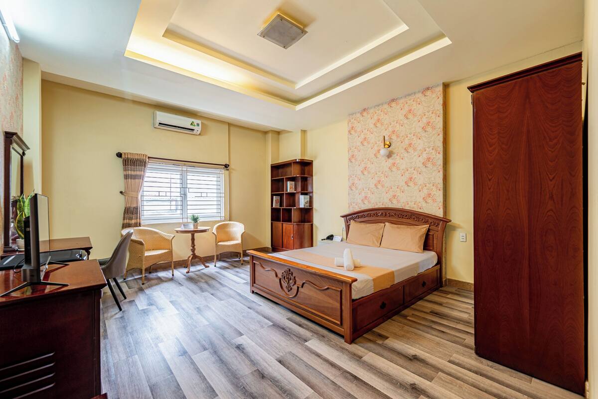 A bedroom with a wooden bed, a desk with a computer, a chair, a small table, and a bookshelf.