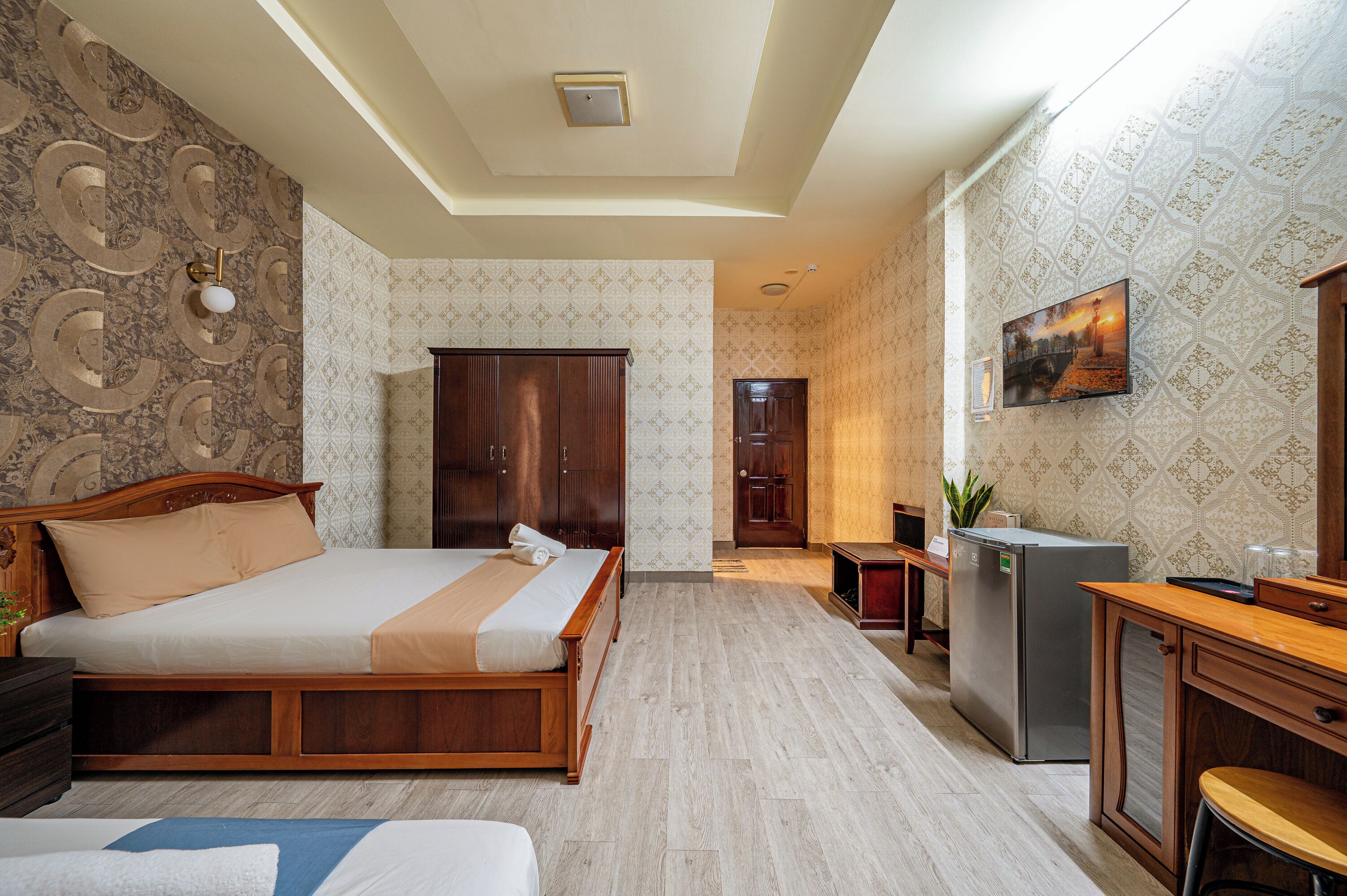A bedroom with a wooden bed, a desk, a refrigerator, and a TV.