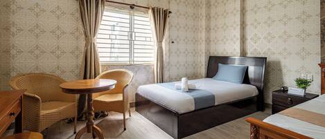 A hotel room with a bed, a chair, a small table, and a window with curtains.