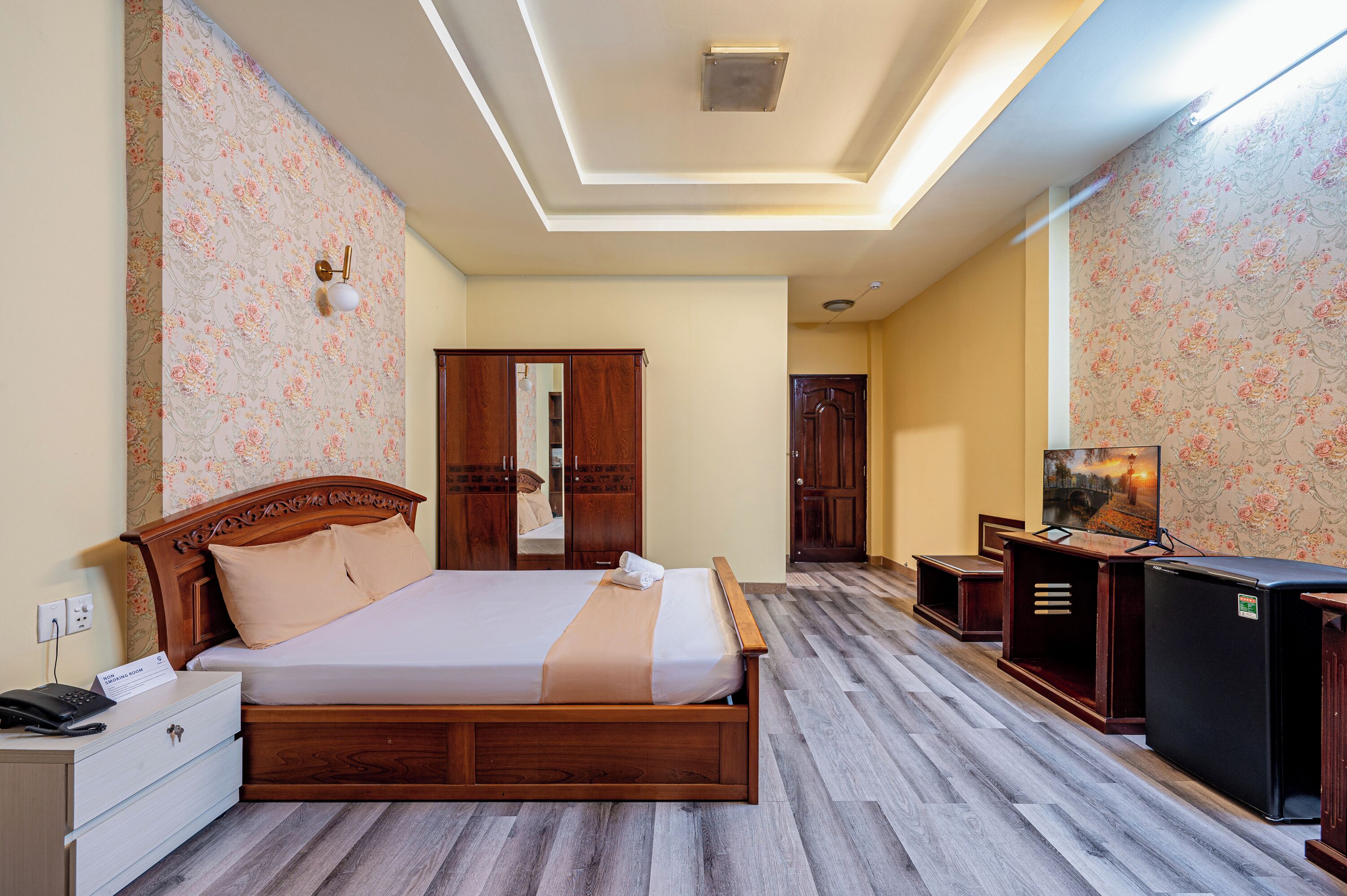 A hotel room with a wooden bed, a desk with a telephone, a television, and a wardrobe.