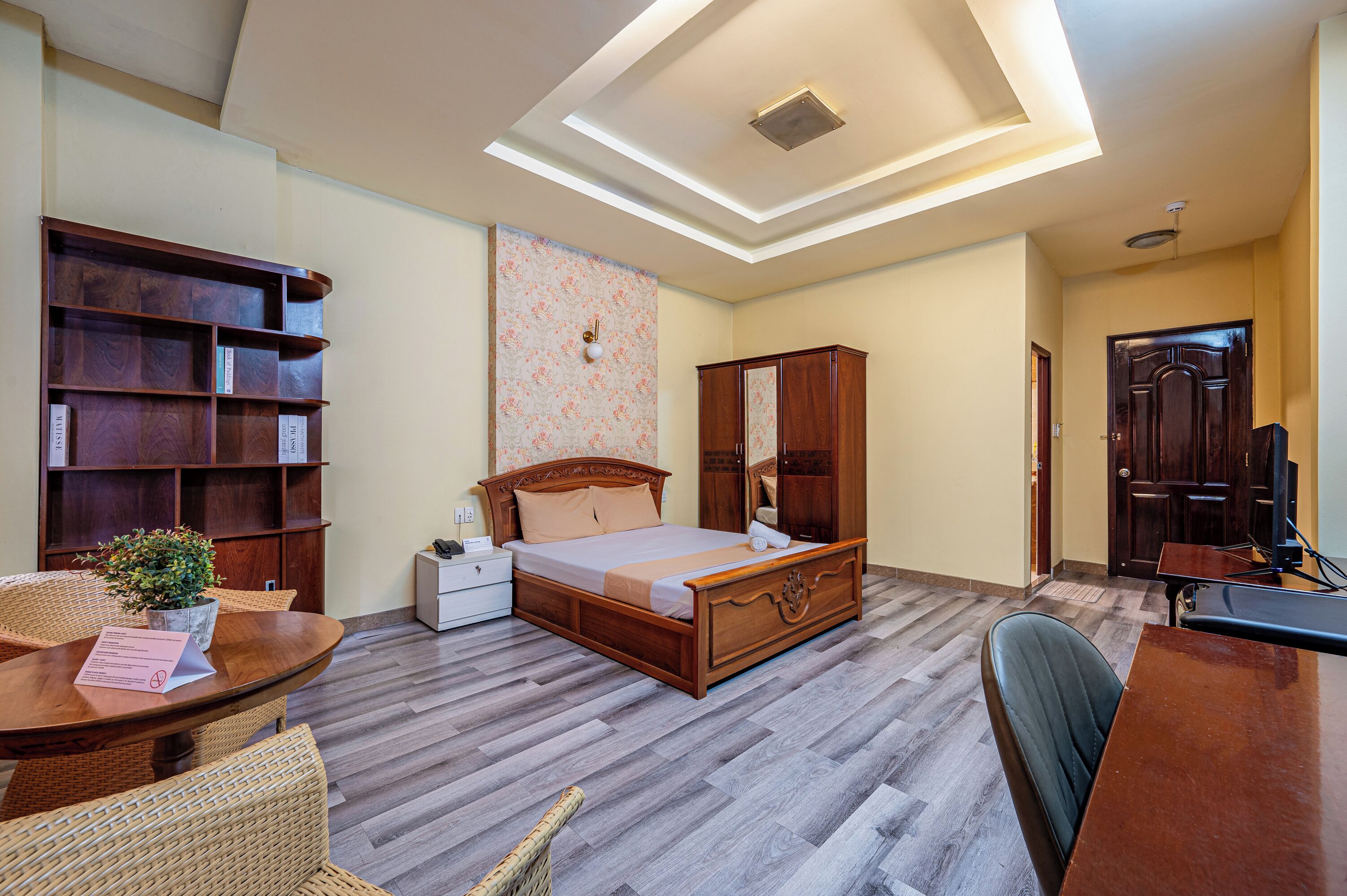 Une chambre à coucher avec un lit en bois, une table de chevet, un bureau, une chaise, une bibliothèque et une plante en pot.