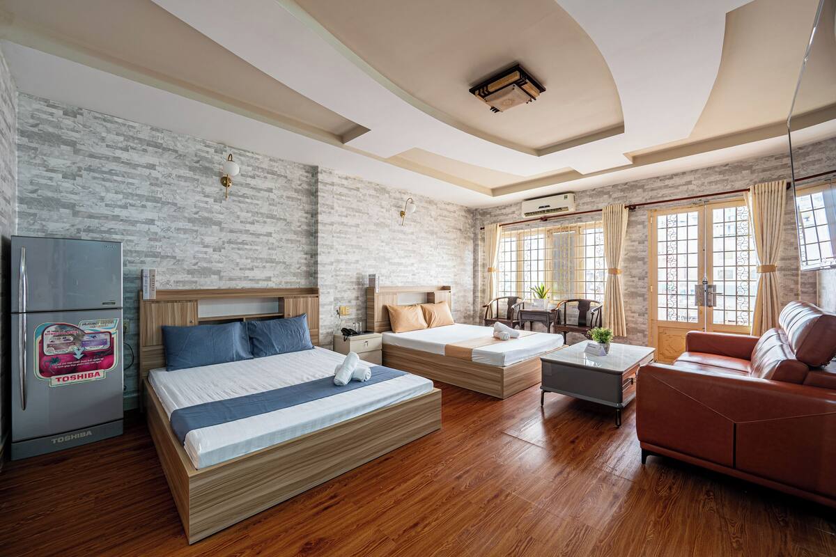 A modern hotel room with a brick wall, wooden flooring, a bed, a sofa, a coffee table, and a refrigerator.