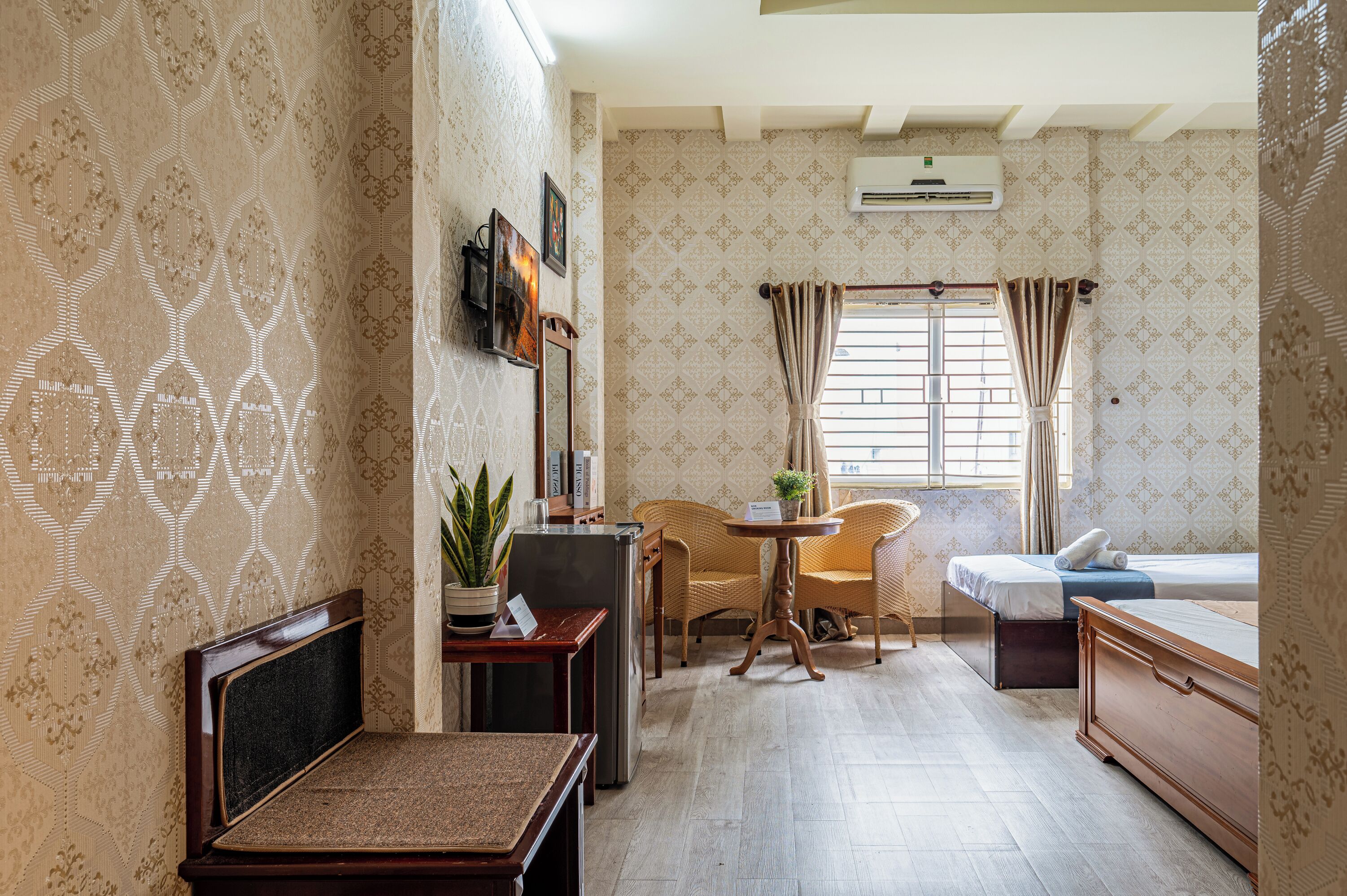 Una habitación de hotel con una cama, una mesita con una planta, una silla, un sofá y un escritorio con una computadora.