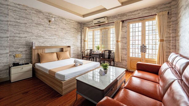 Habitación de hotel con cama, sofá, escritorio y silla. Se ve una ventana con cortinas y un equipo de aire acondicionado en la pared.