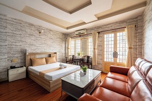 Habitación de hotel con cama, sofá, escritorio y silla. Se ve una ventana con cortinas y un equipo de aire acondicionado en la pared.