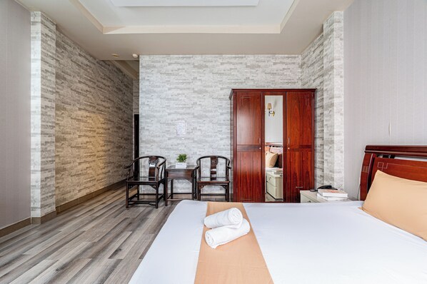 Habitación de hotel con una cama grande, un armario de madera, dos sillas, una mesita y un espejo.