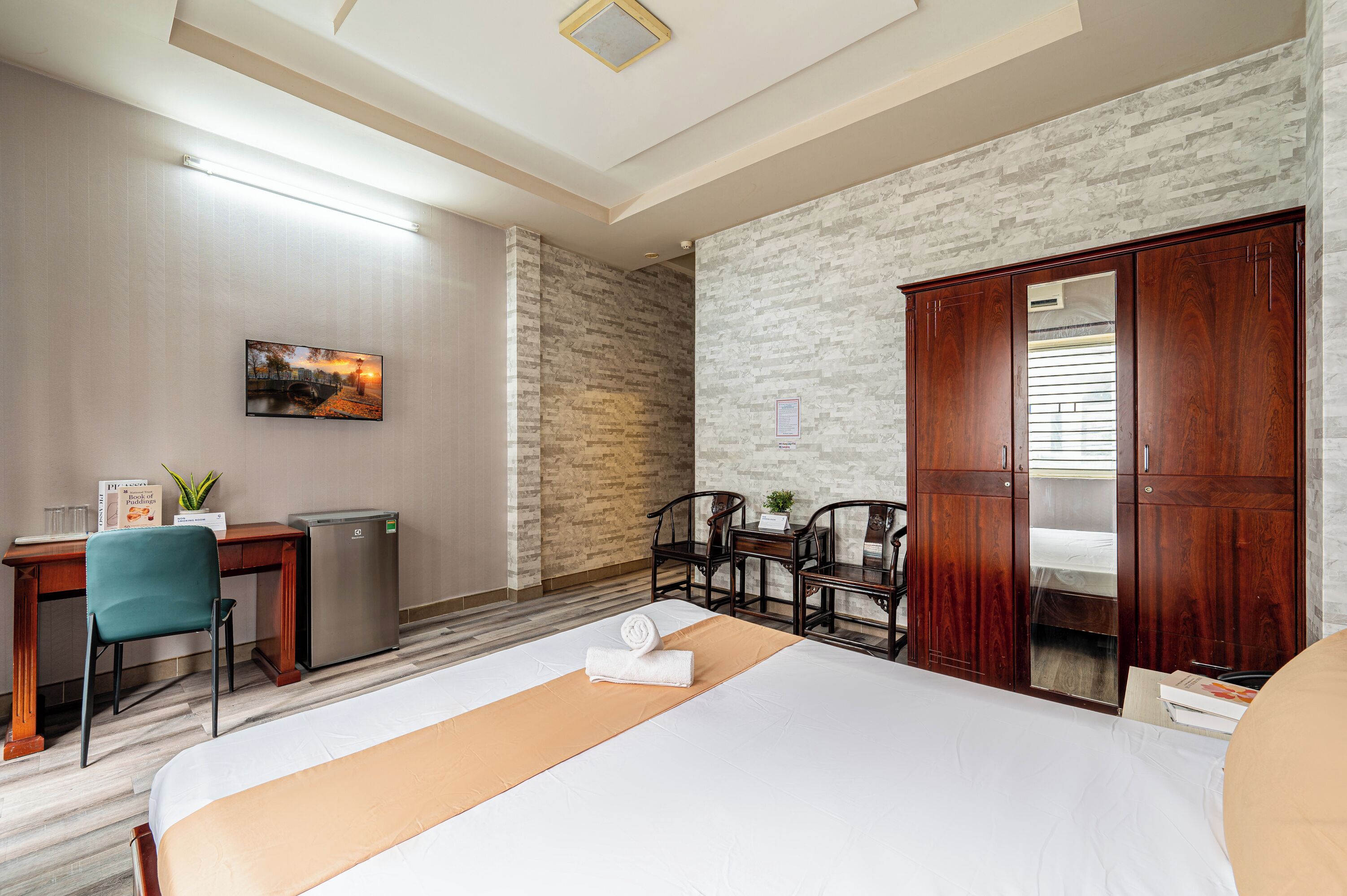 A hotel room with a bed, desk, refrigerator, and wardrobe.