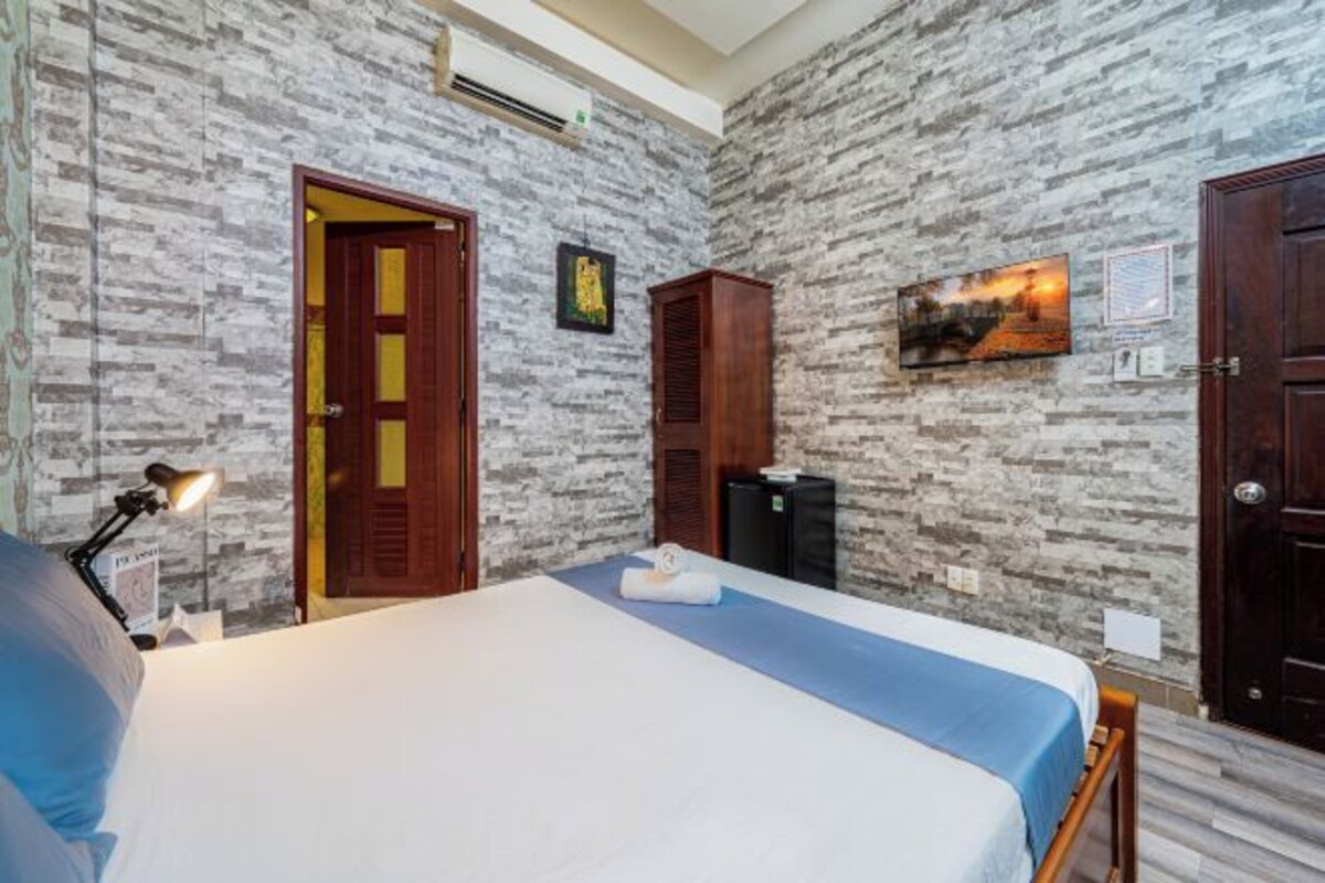 A hotel room with a bed, a desk with a lamp, a wardrobe, and a wall-mounted TV.