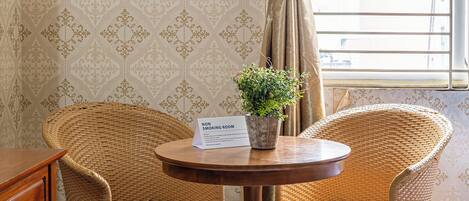 Une chambre non-fumeur avec deux fauteuils en osier, une petite table sur laquelle est posée une plante en pot, et une fenêtre avec des rideaux.