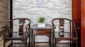 Una habitación con pared de piedra, dos sillas de madera, una mesita con una planta y un armario de madera.
