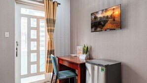 Una habitación con un escritorio de madera, una silla, un refrigerador pequeño y un televisor en la pared.