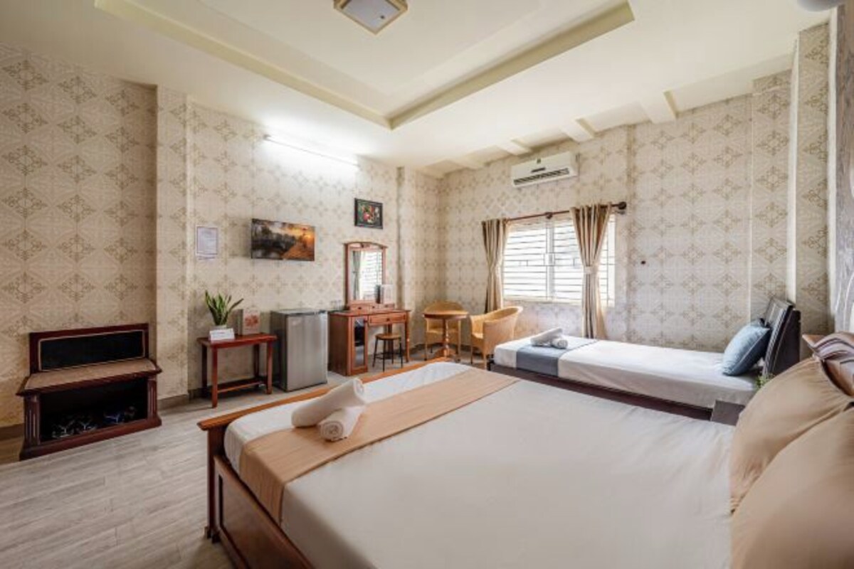 A hotel room with a large bed, a desk, a chair, a small table, and a television.