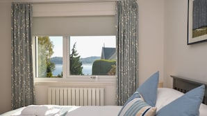 A bedroom with a bed, a window with curtains, a radiator, and a framed picture on the wall.