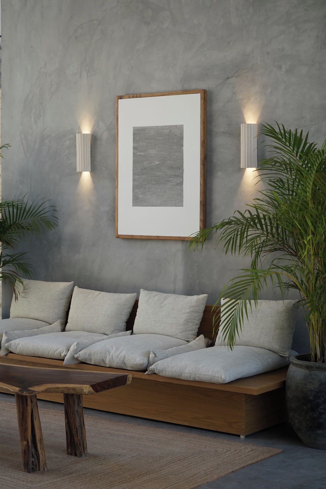 Una sala de estar moderna con un sofá, dos luces empotradas, un cuadro enmarcado y plantas en macetas.