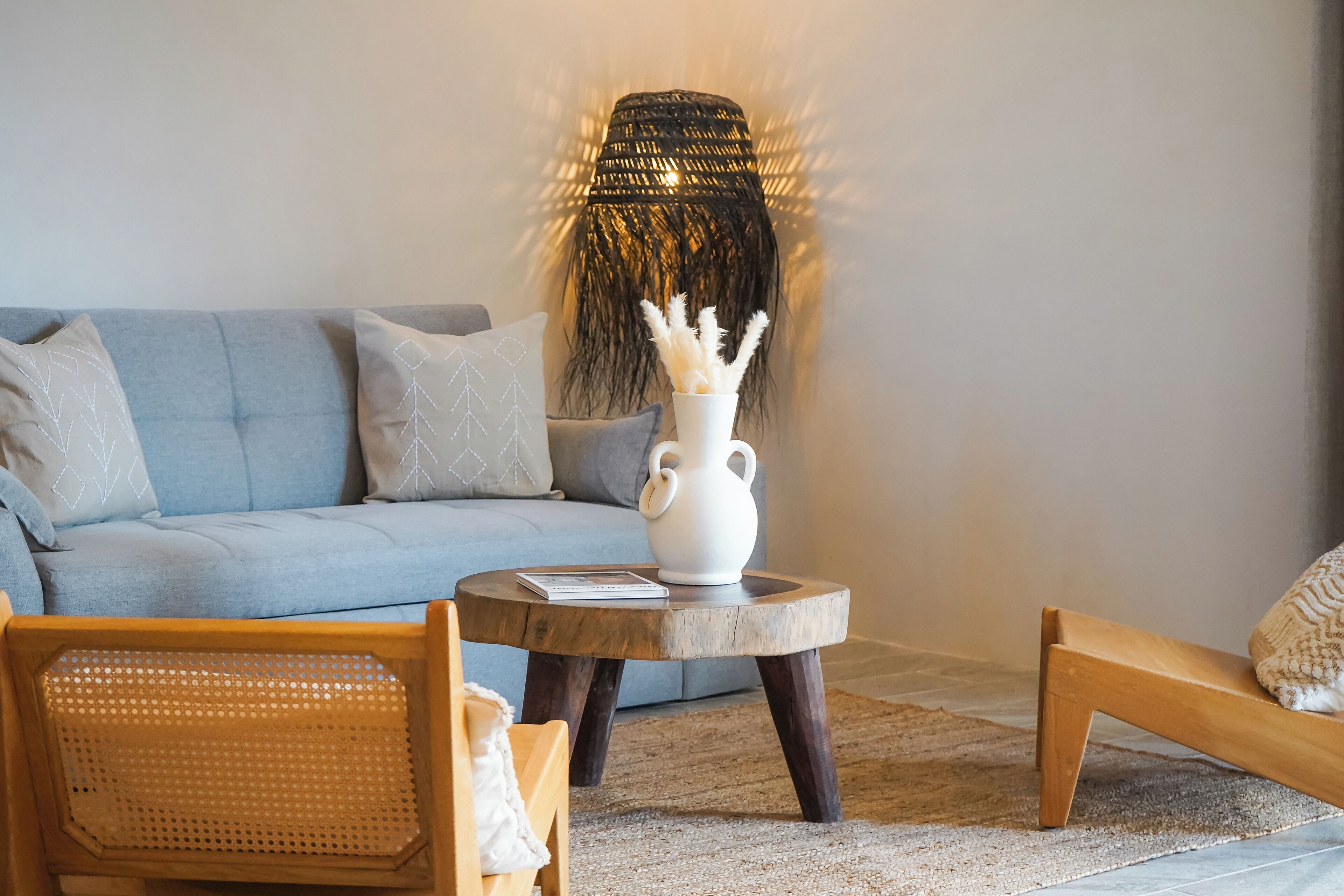 A living room with a light blue sofa, a round wooden coffee table with a white vase, and a wicker chair.