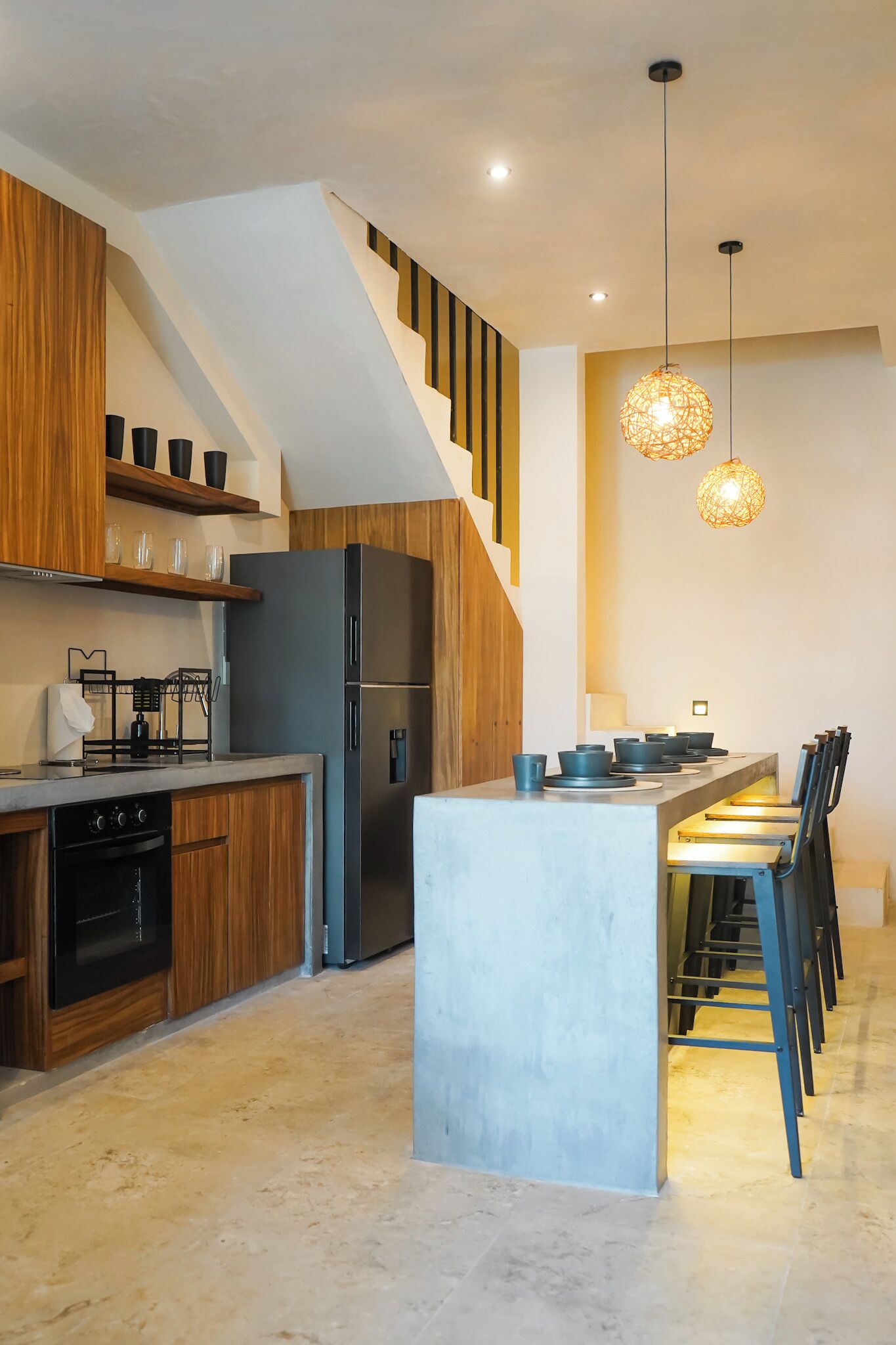 Une cuisine moderne dotée d’un îlot central, de meubles en bois, d’un four encastré et d’un réfrigérateur noir.
