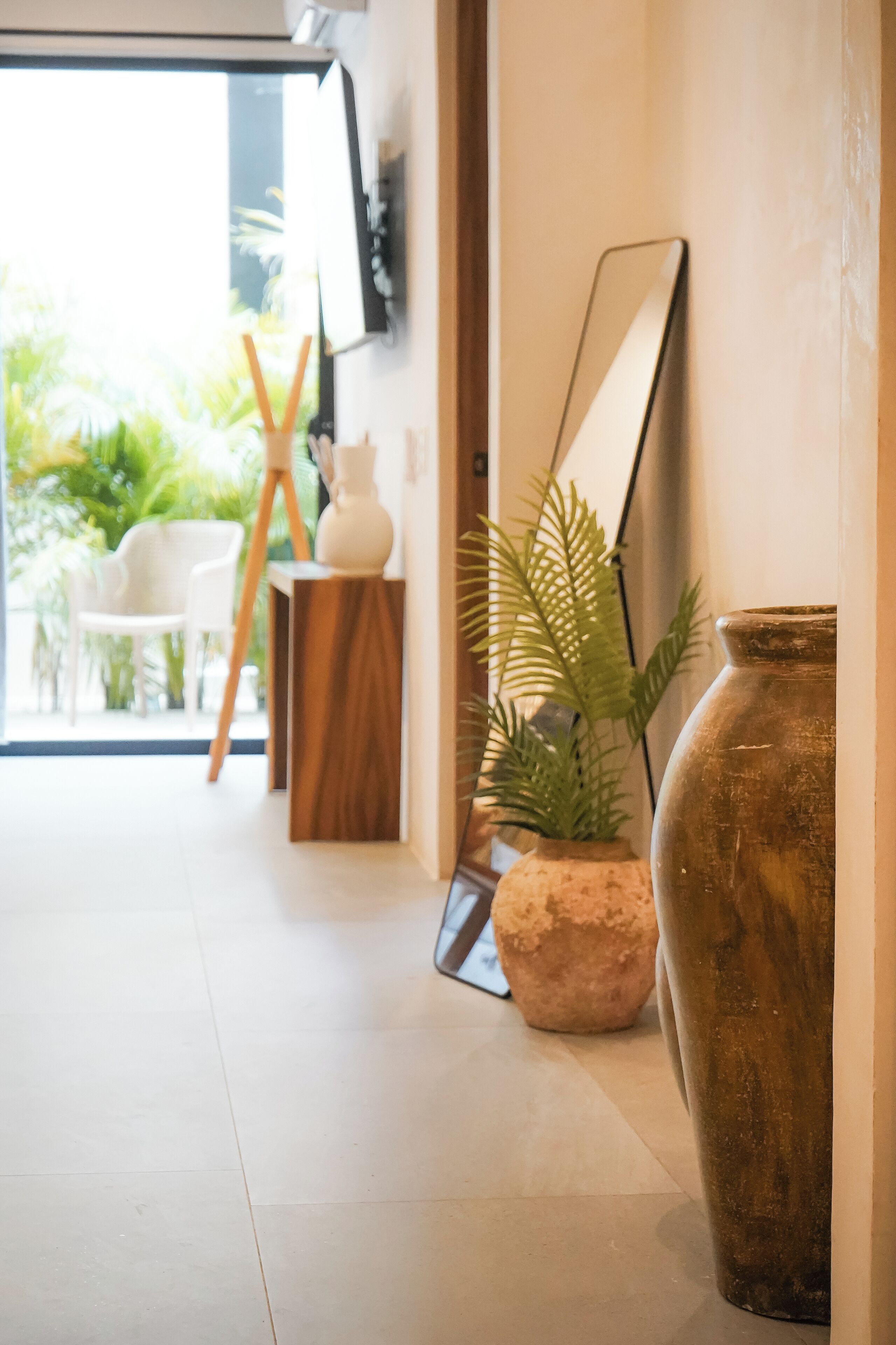 A hallway with a large mirror, a wooden side table, a potted plant, and a rustic vase.