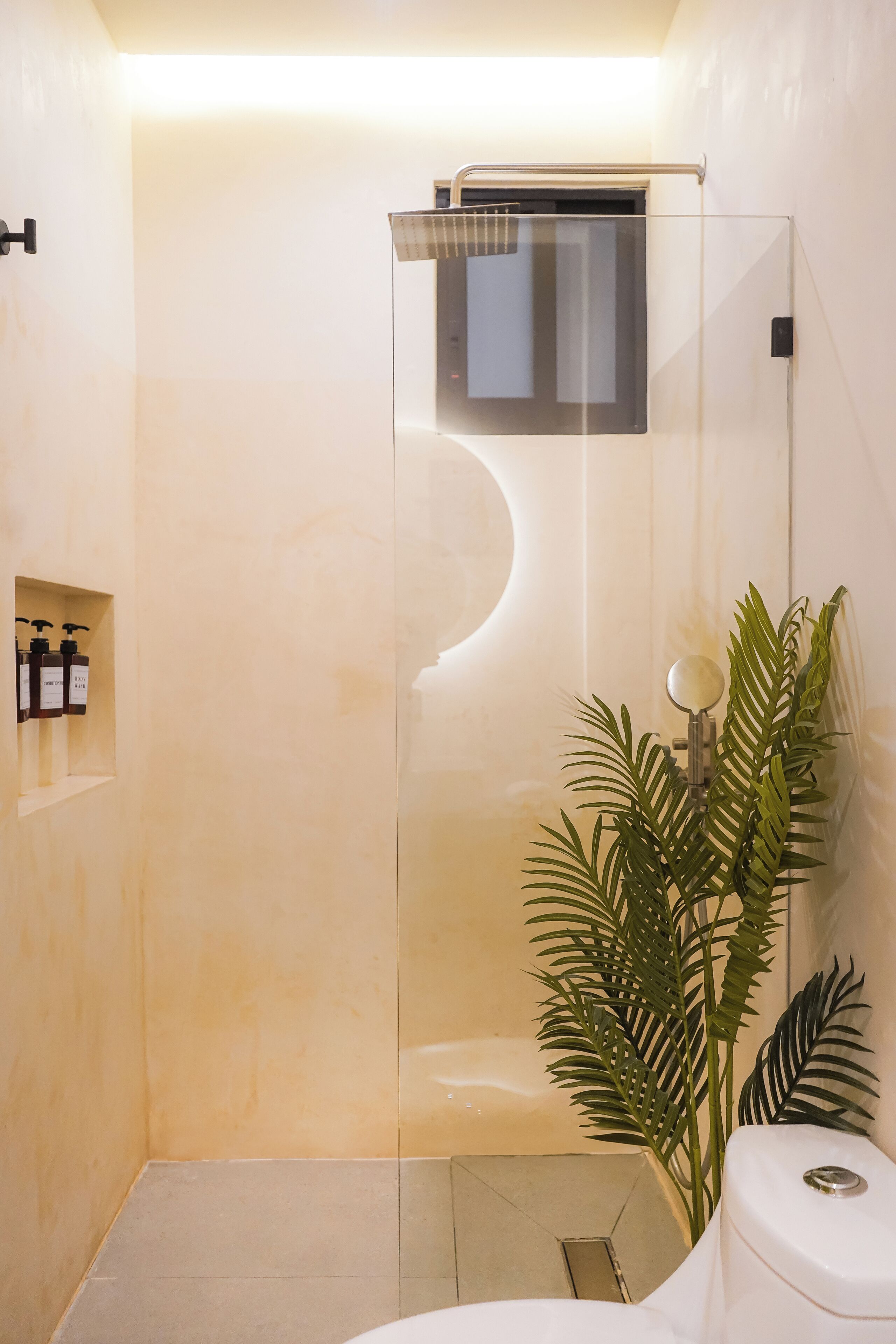 Een moderne badkamer met een douche met glazen wand, een toilet en een plant in pot.