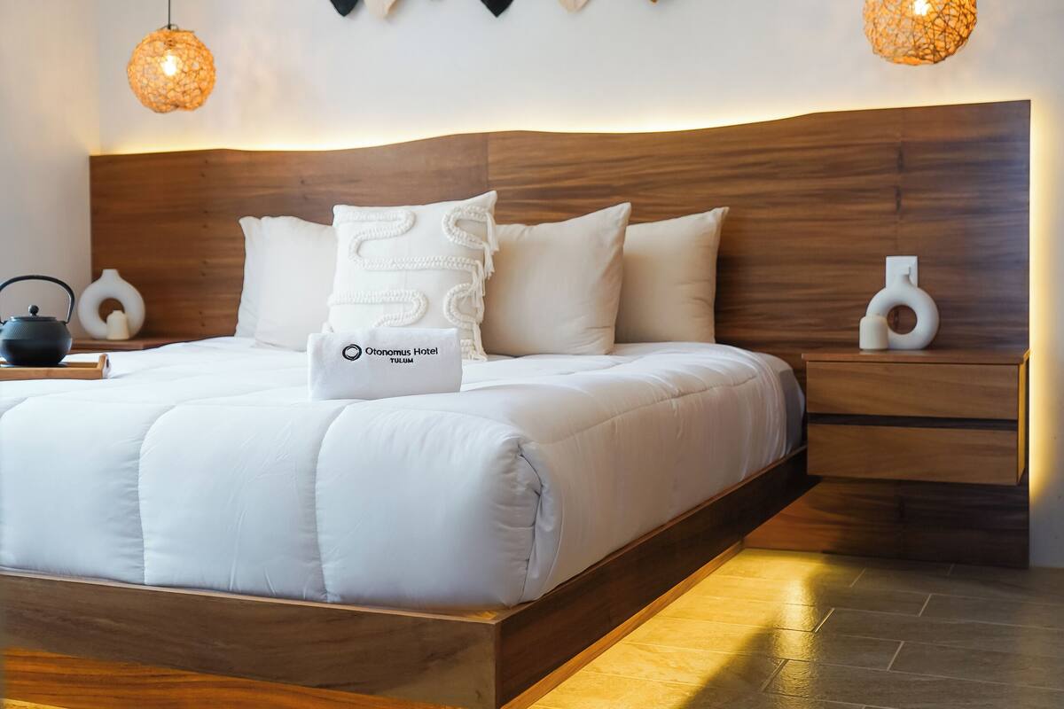 A modern bedroom with a wooden headboard, a white bedspread, and a hanging leaf decoration.