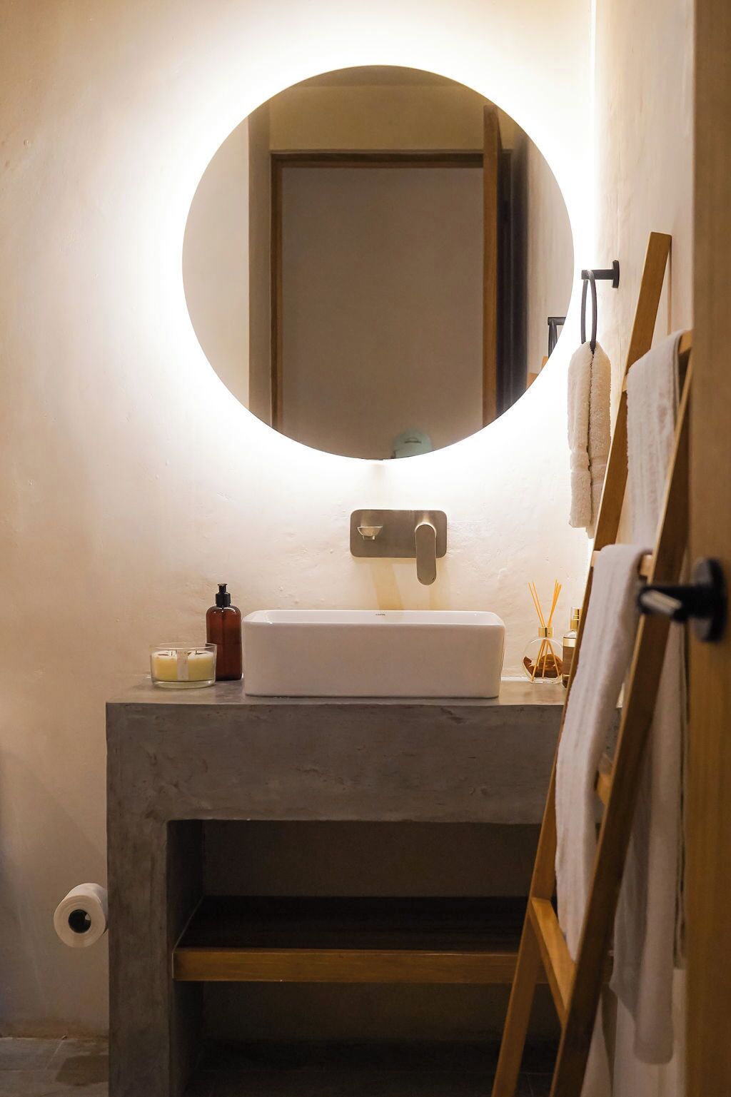 A bathroom with a round mirror, a white sink, and a wooden easel with a painting.
