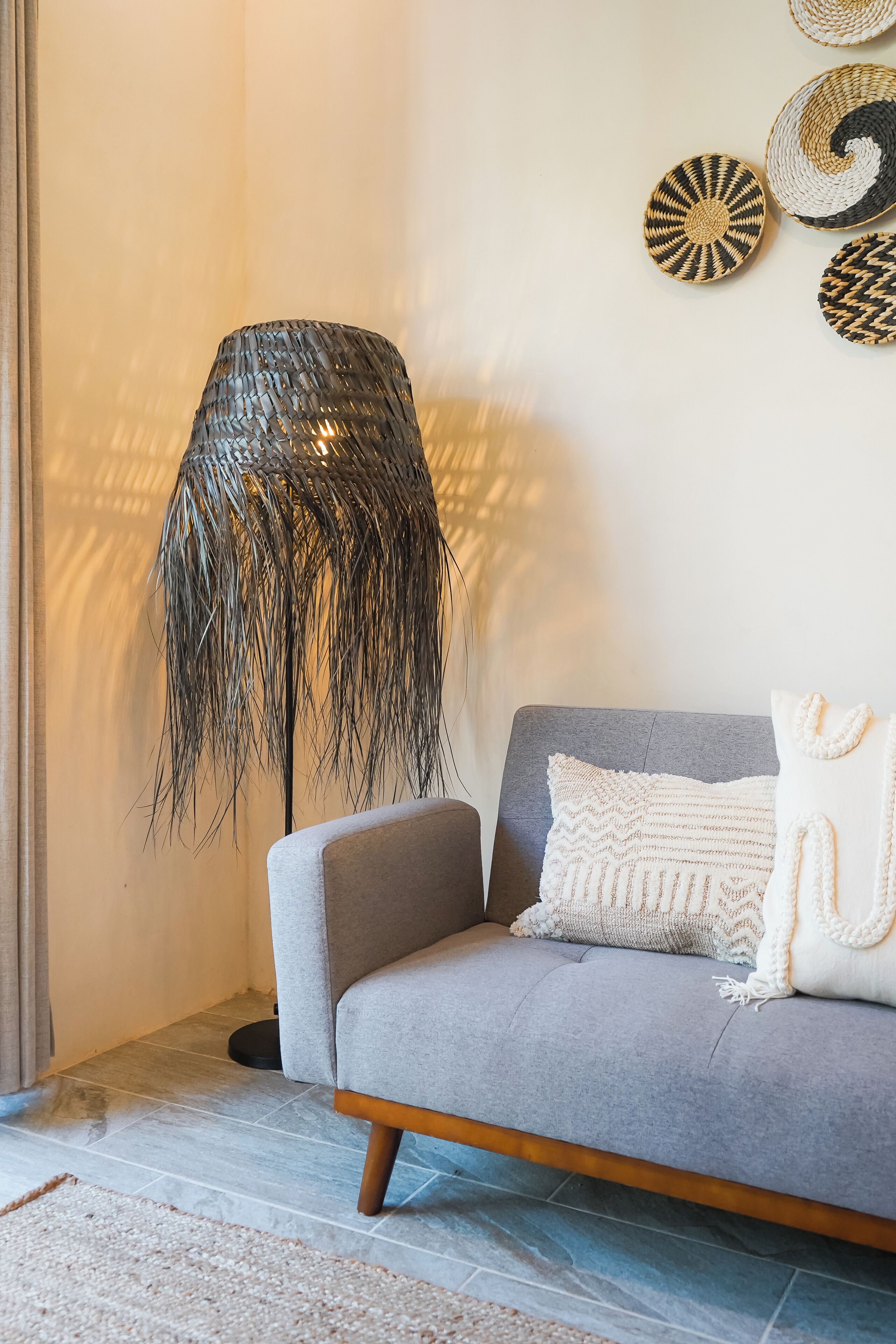 A modern living room with a grey sofa, a woven floor lamp, and decorative woven wall art.