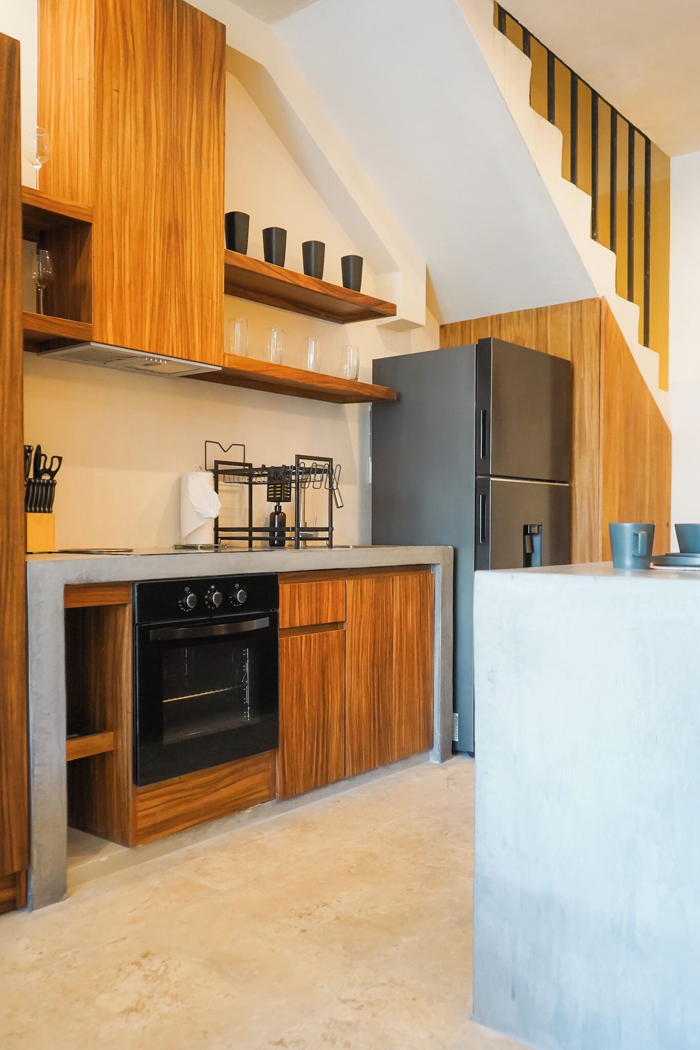 Una cocina moderna con armarios de madera, horno empotrado, estufa a gas y refrigerador negro.