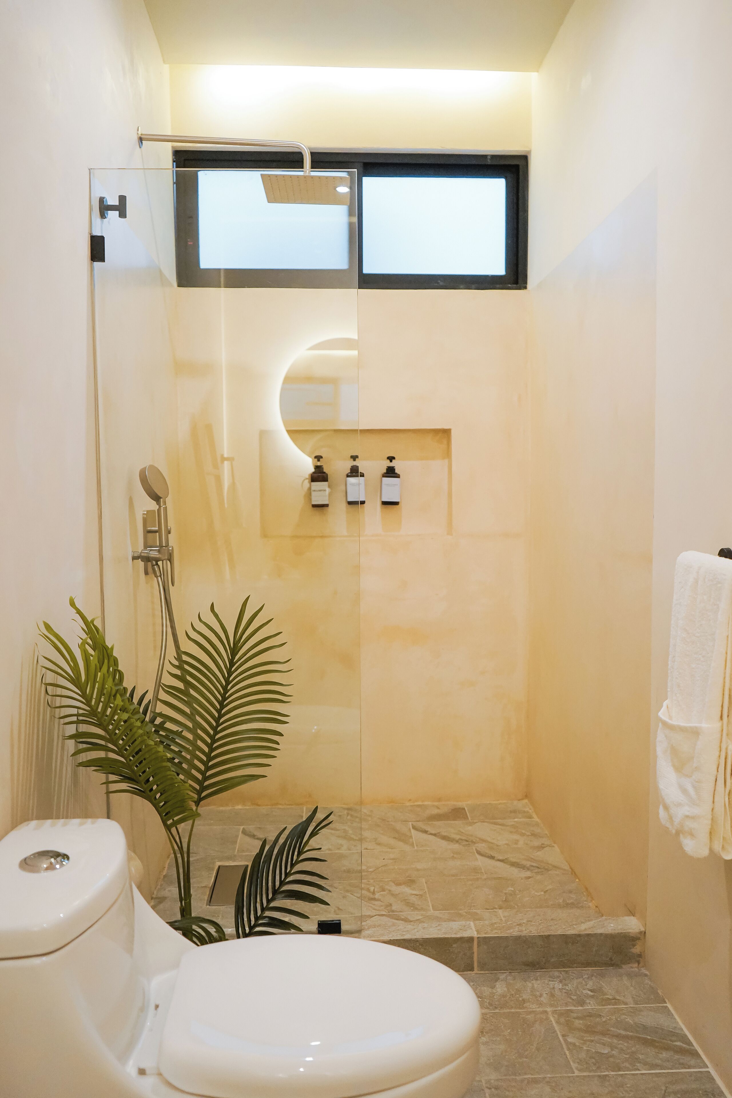 A compact bathroom with a toilet, shower, and a small shelf with toiletries.