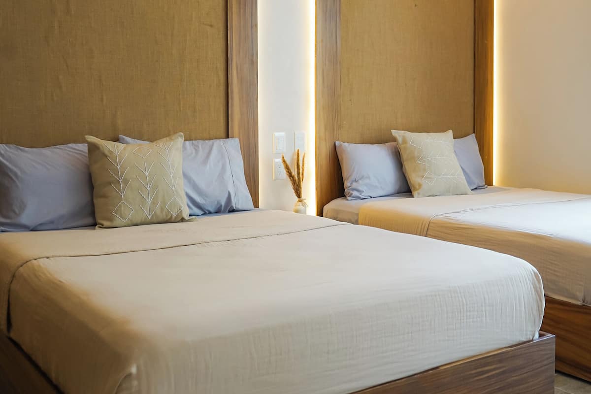 A modern hotel room with two beds, wooden headboards, and a neutral color scheme.