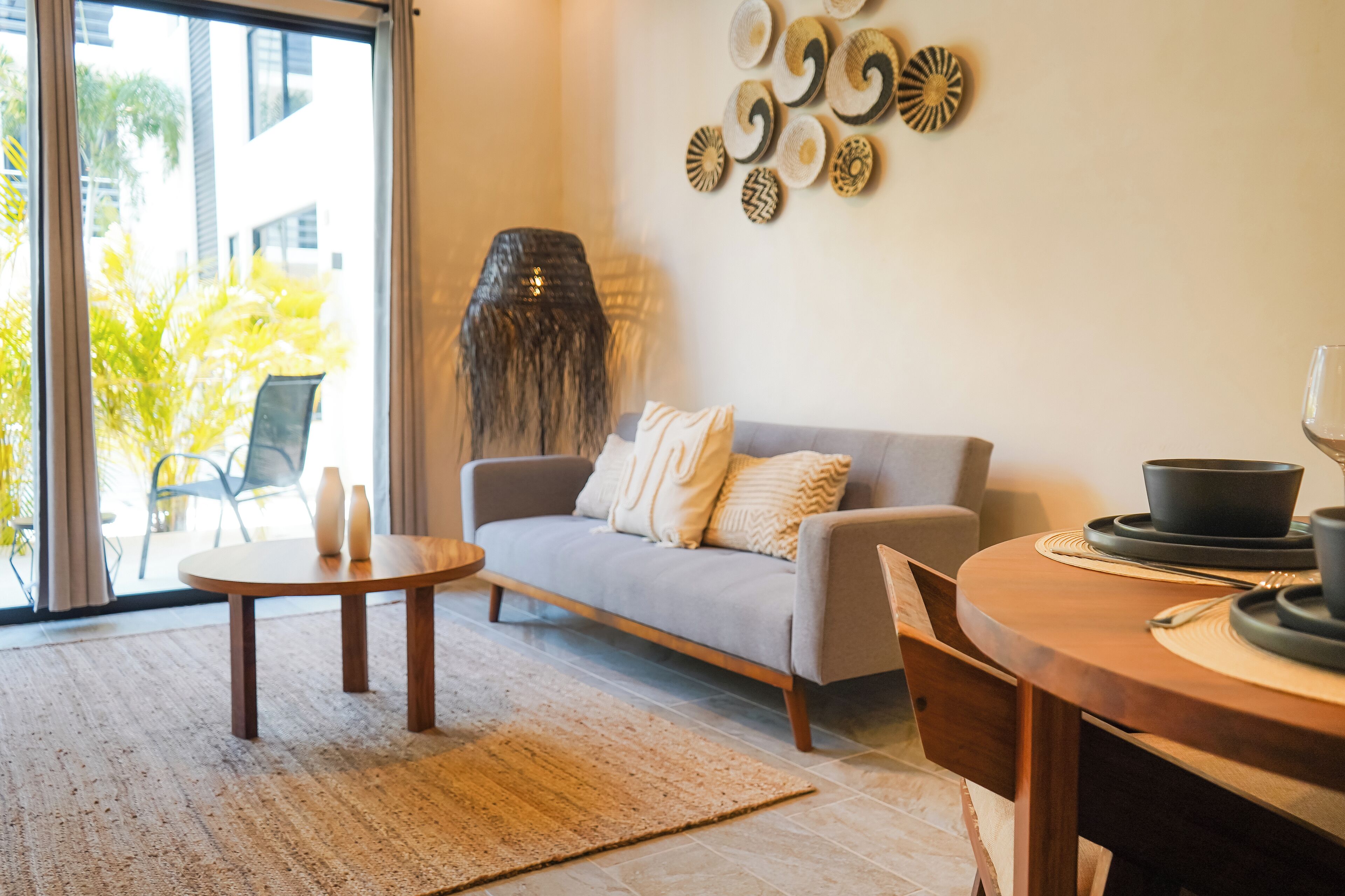 A modern living room with a grey sofa, a wooden coffee table, and a dining table with a bowl and cup.