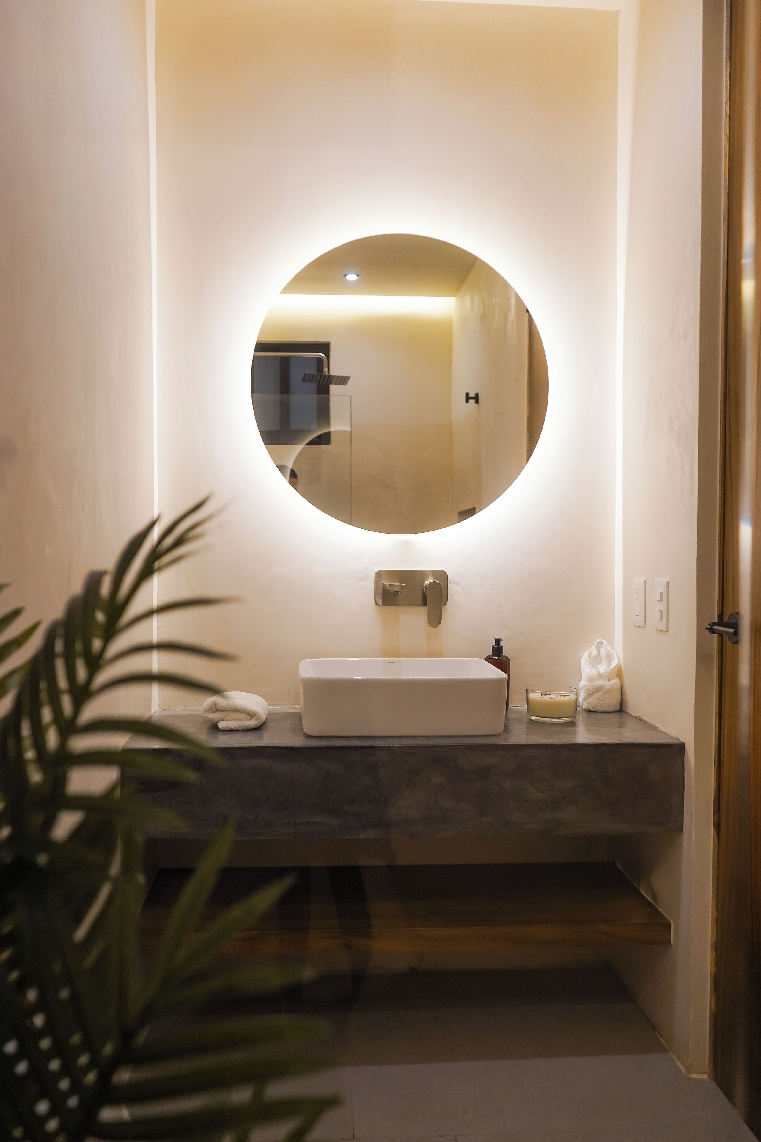 Une salle de bain moderne avec un miroir rond, un lavabo blanc et une petite plante.