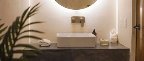 Une salle de bain moderne avec un miroir rond, un lavabo blanc et une petite plante.