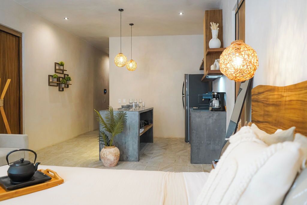 A modern hotel room with a bed, a small kitchenette, a dining area, and a living space.