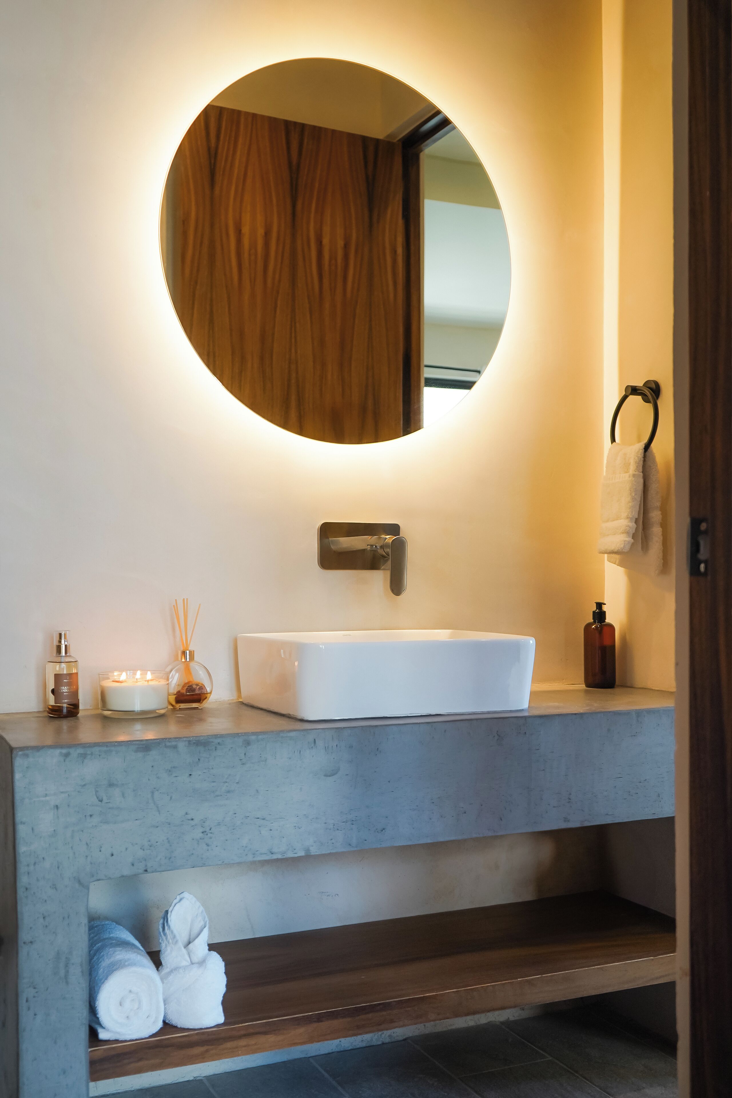A bathroom with a round mirror, white sink, and wooden vanity.