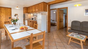 A kitchen with wooden cabinets, a dining table set for four, and a small seating area with a sofa and a table with a newspaper. - Gites Simond welcomes you to Arvieux in the heart of the Queyras Regional Park, (Arvieux)