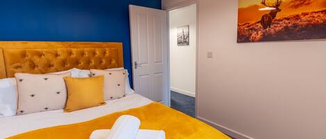 A hotel room with a bed, a painting of a deer, and a door leading to another room.