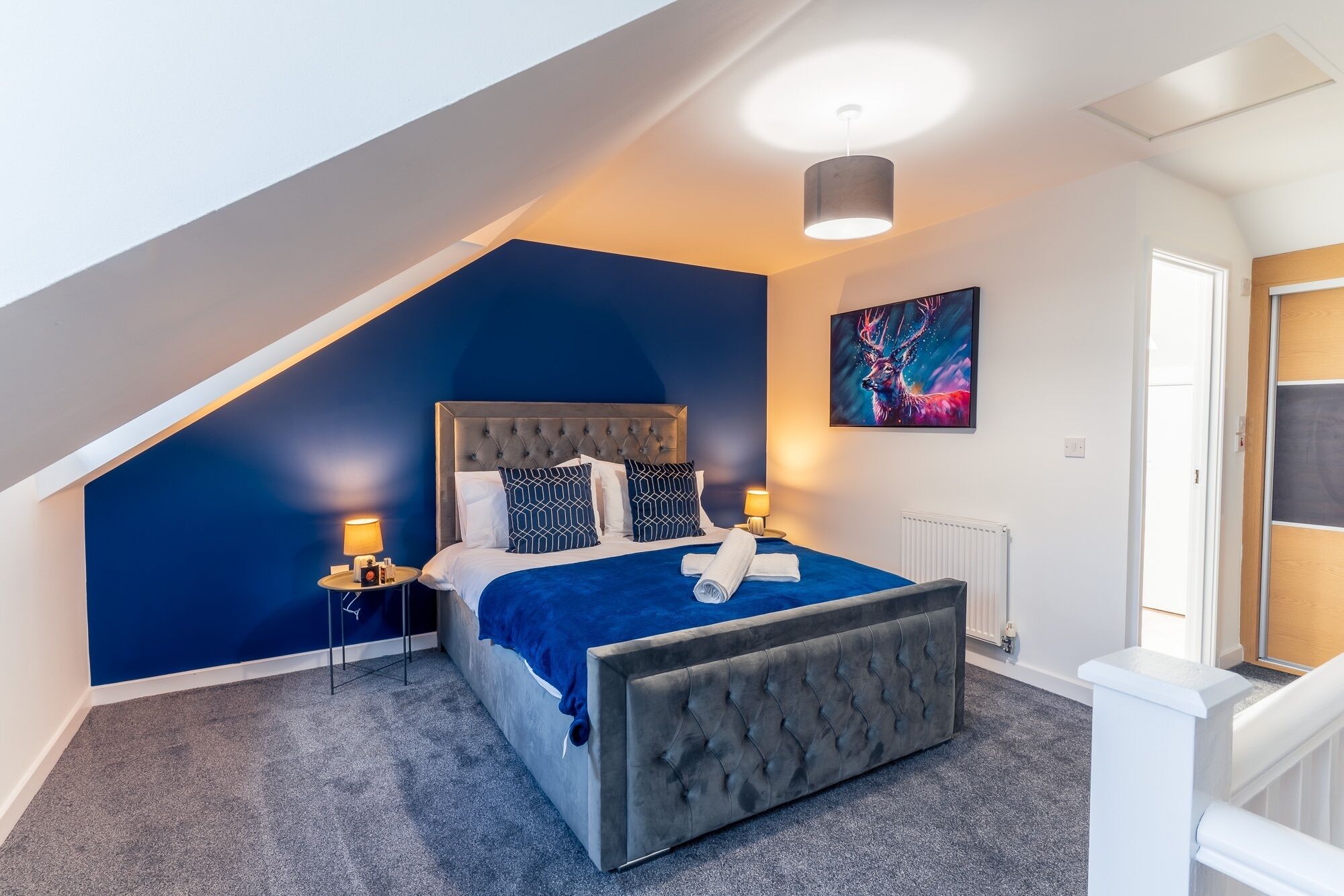 Une chambre avec un plafond en pente, un lit à capitonnage, un radiateur et un tableau accroché au mur.