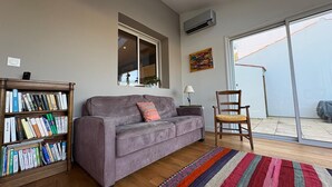 Ein Wohnzimmer mit grauem Sofa, einer Bücherwand, einem farbenfrohen Teppich und einem Fenster mit Blick.