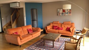 A living room with two orange sofas, a wooden coffee table, a patterned rug, a staircase, and a modern art piece on the wall.