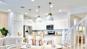 A modern kitchen with white cabinets, stainless steel appliances, and pendant lighting.